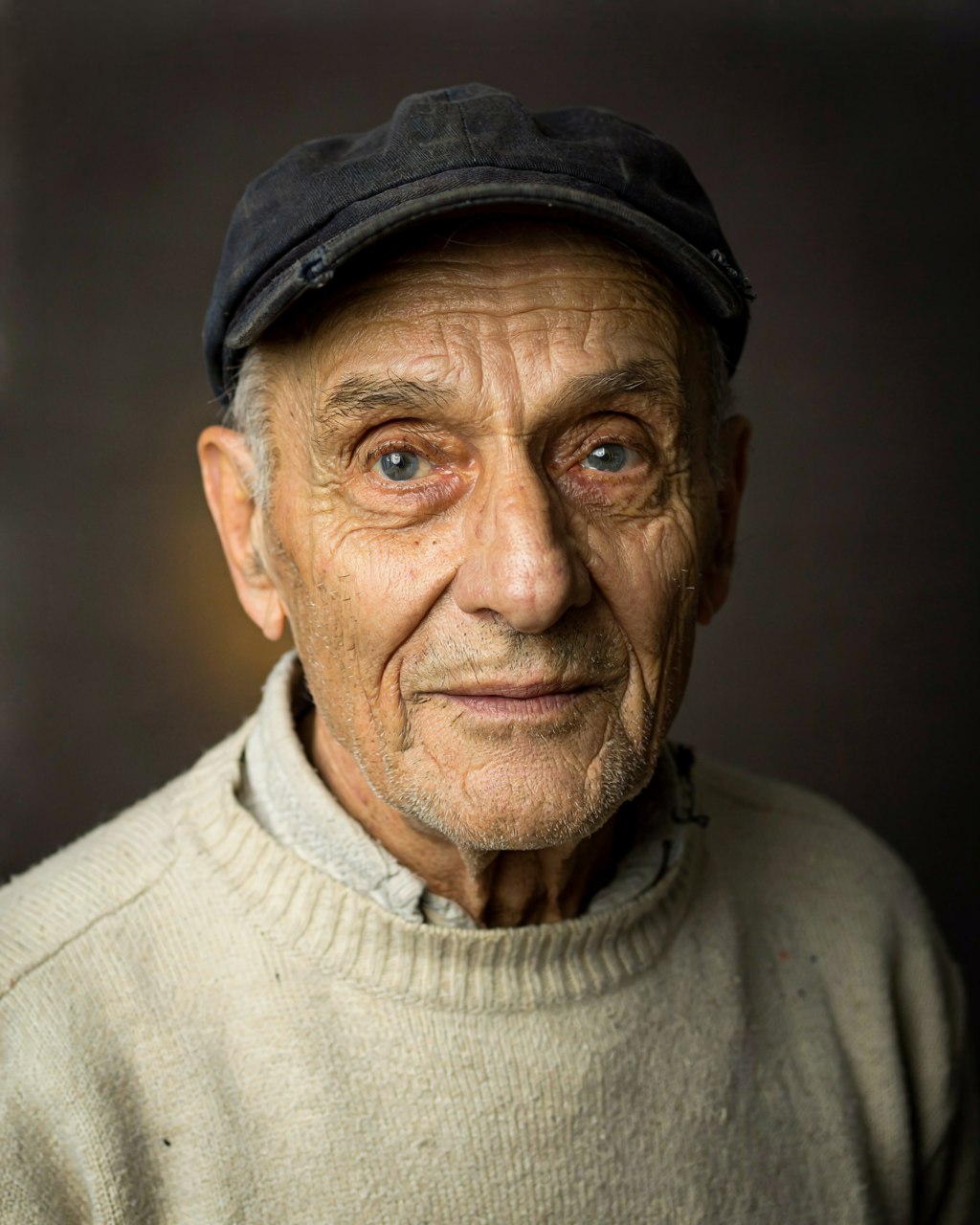Photorealistic studio portrait of an elderly fisherman in a navy cap and cream wool sweater, Rembrandt lighting